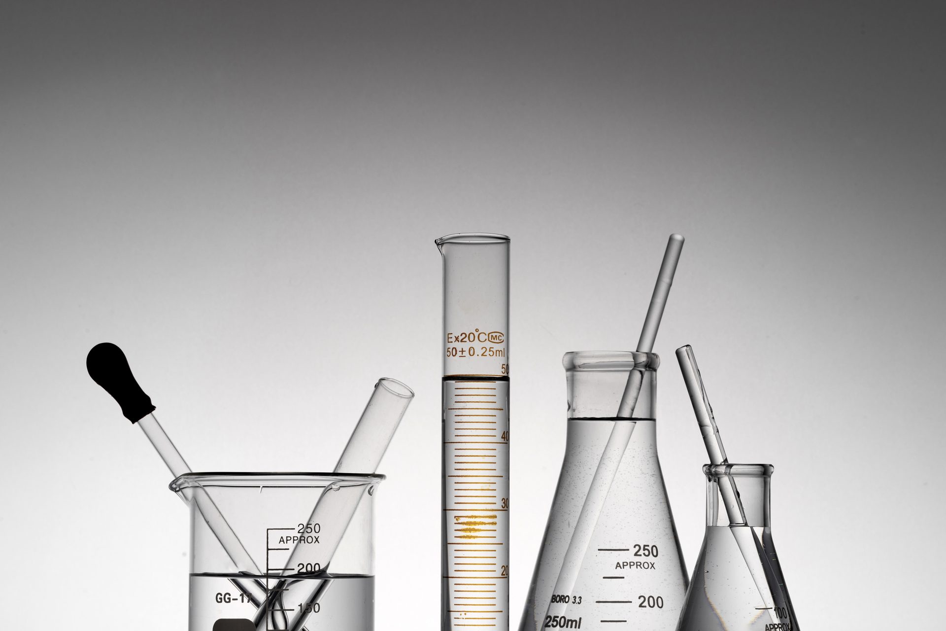 Laboratory glassware with clear liquid: beaker, graduated cylinder and conical flasks on grey