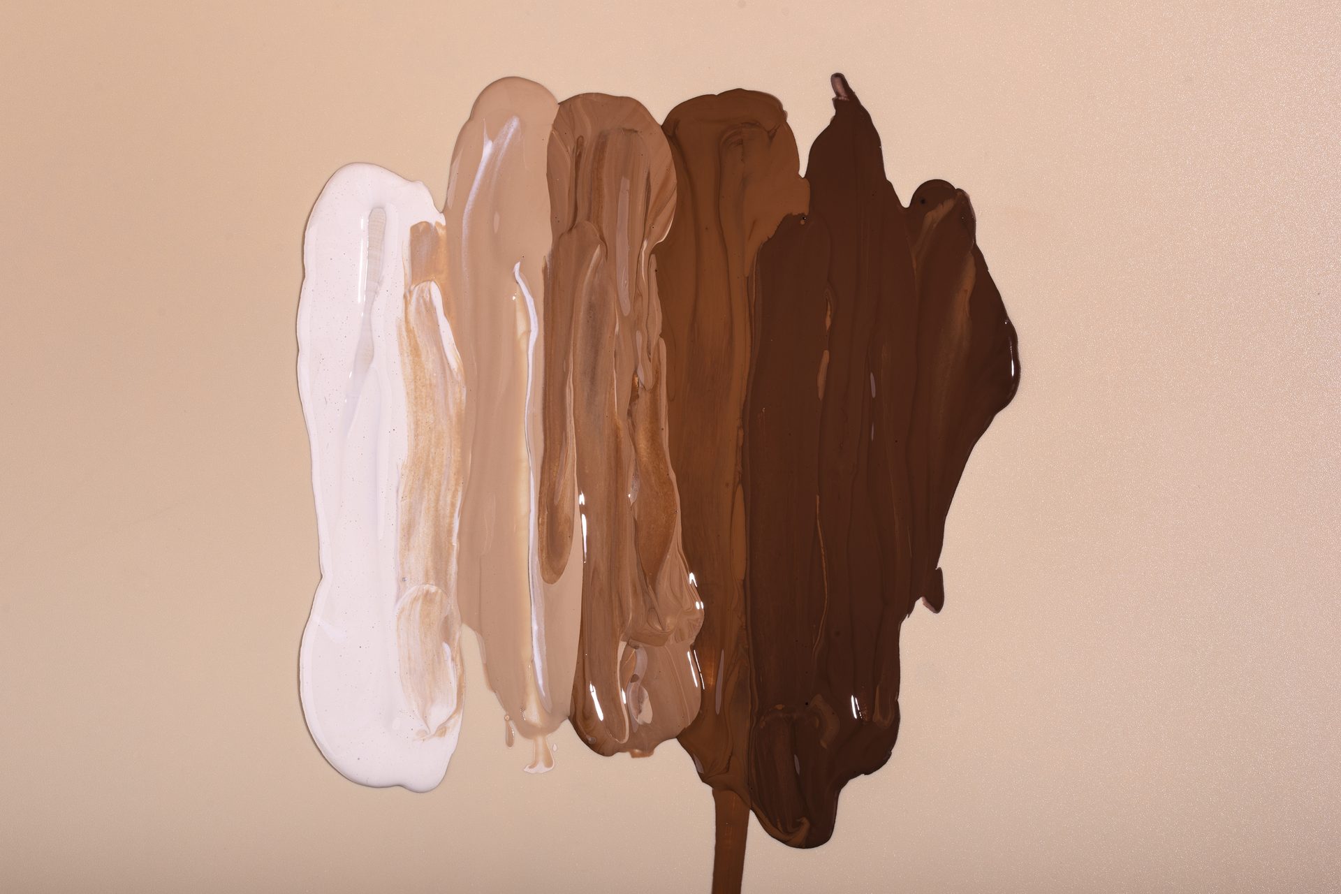 Vertical smears of foundation from white through beige to dark brown on a beige background