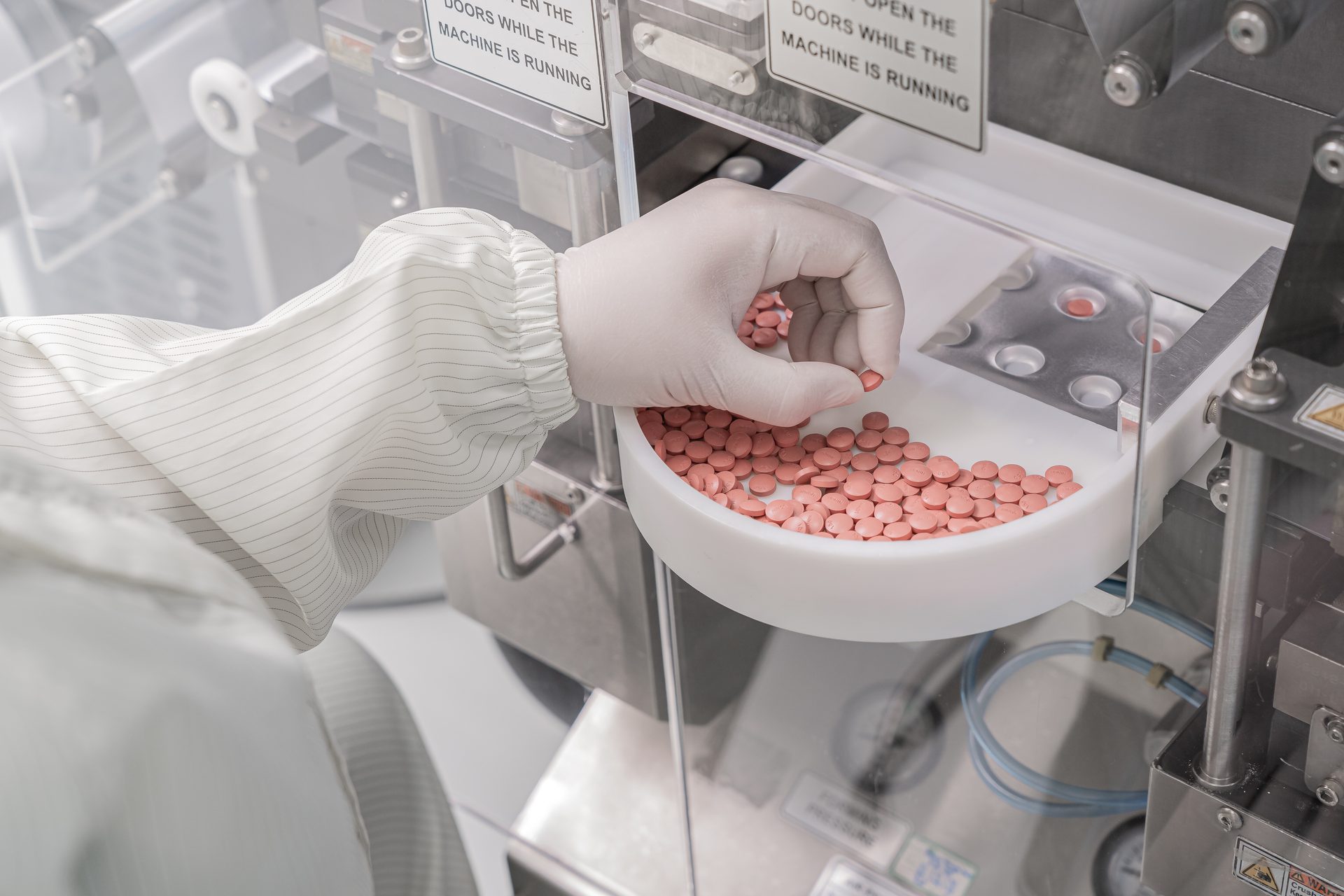 Gloved operator in a white suit picking pink tablets from a tray on a packaging machine