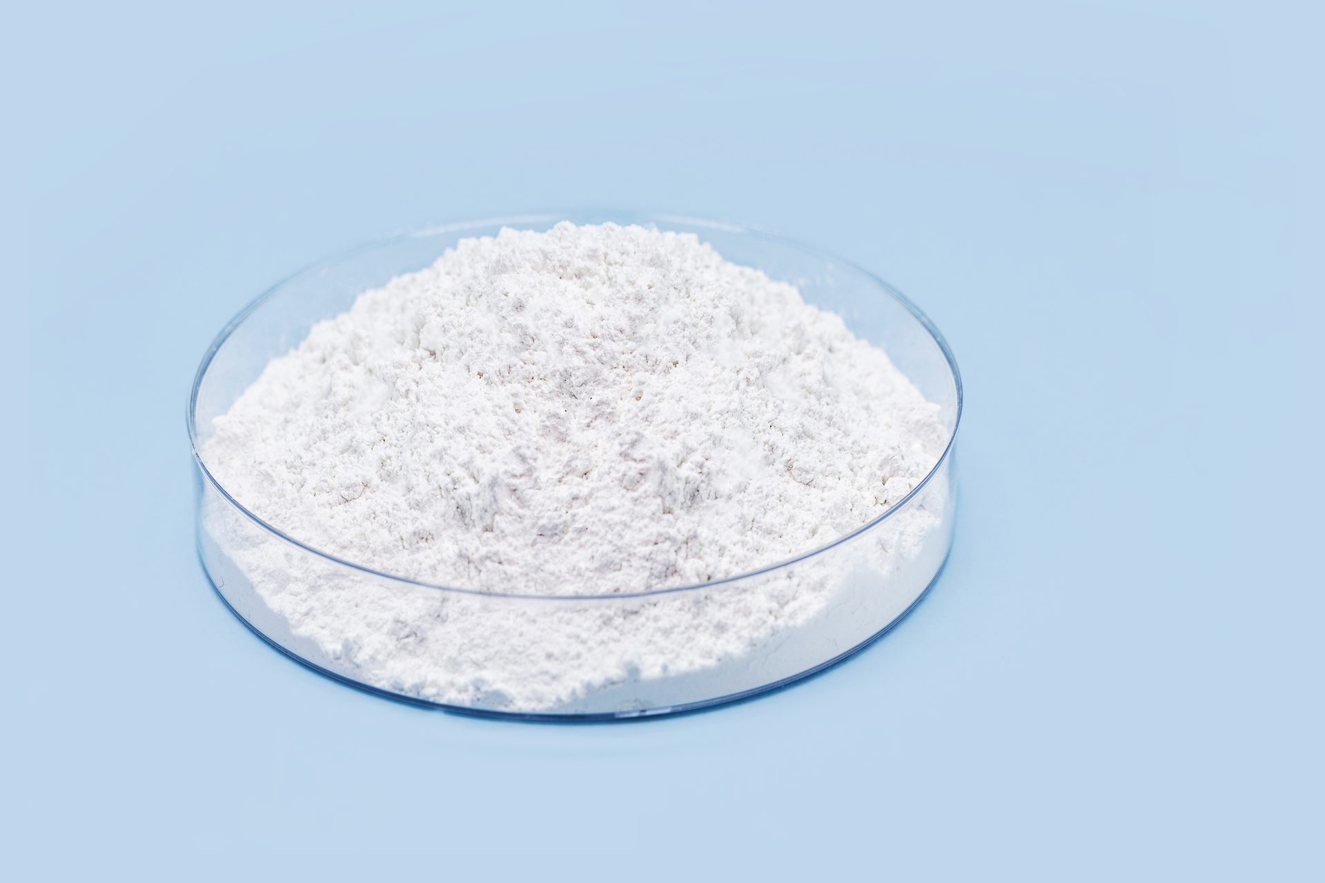 Glass dish heaped with fine white powder on a pale blue background