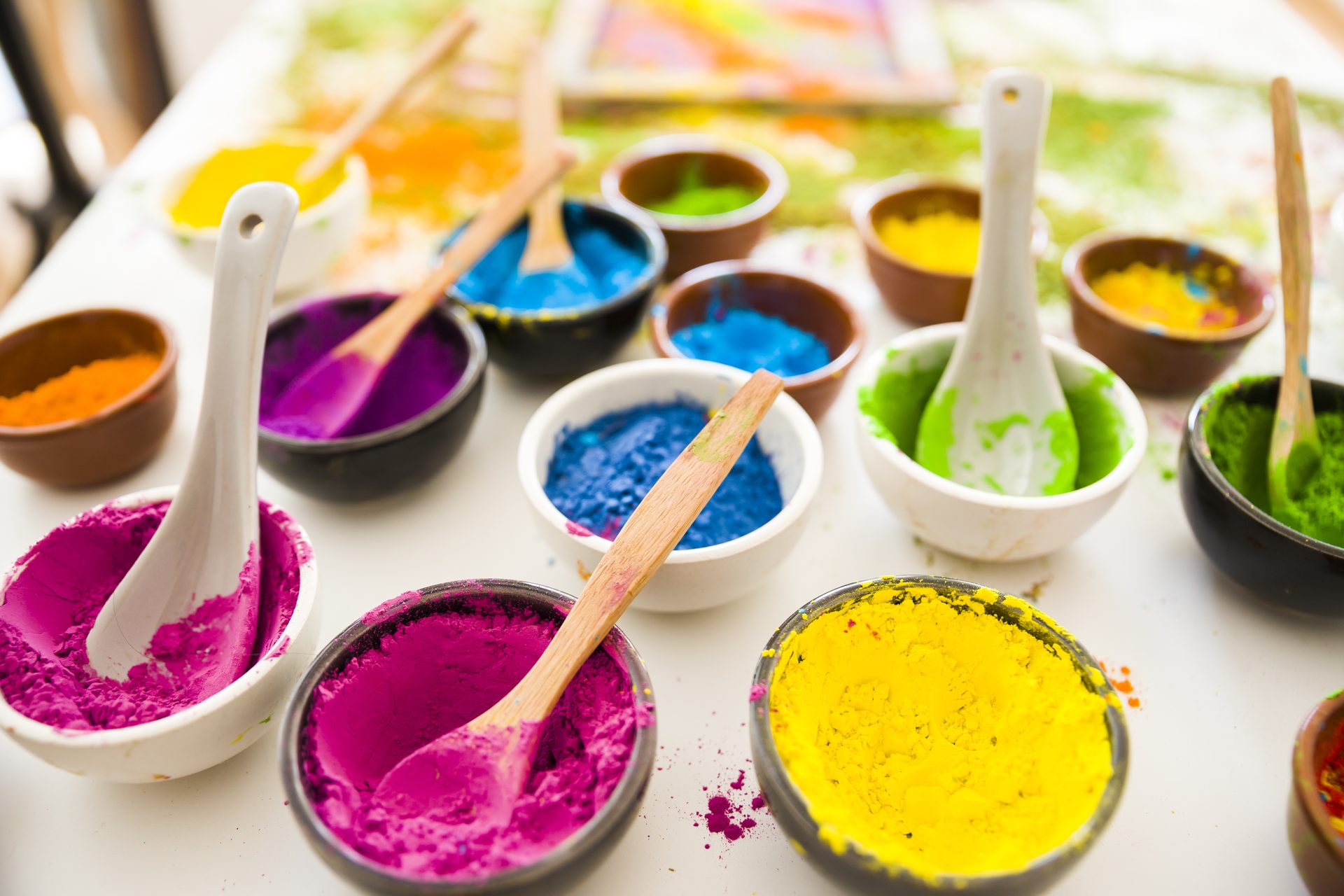 Small bowls of bright pink, blue, yellow, green and orange powder with spoons on a table