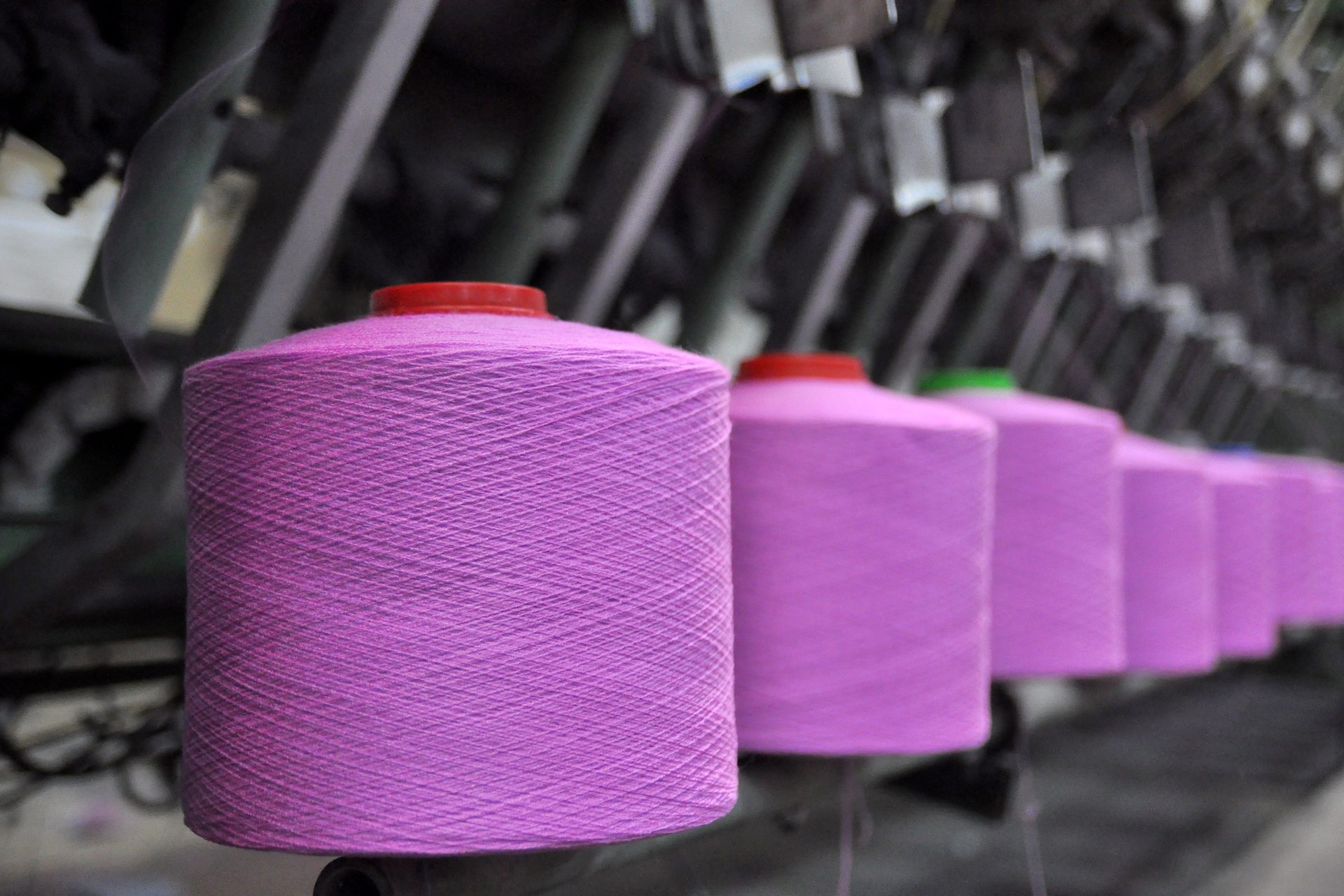 Row of large pink yarn cones mounted on a textile machine in a factory