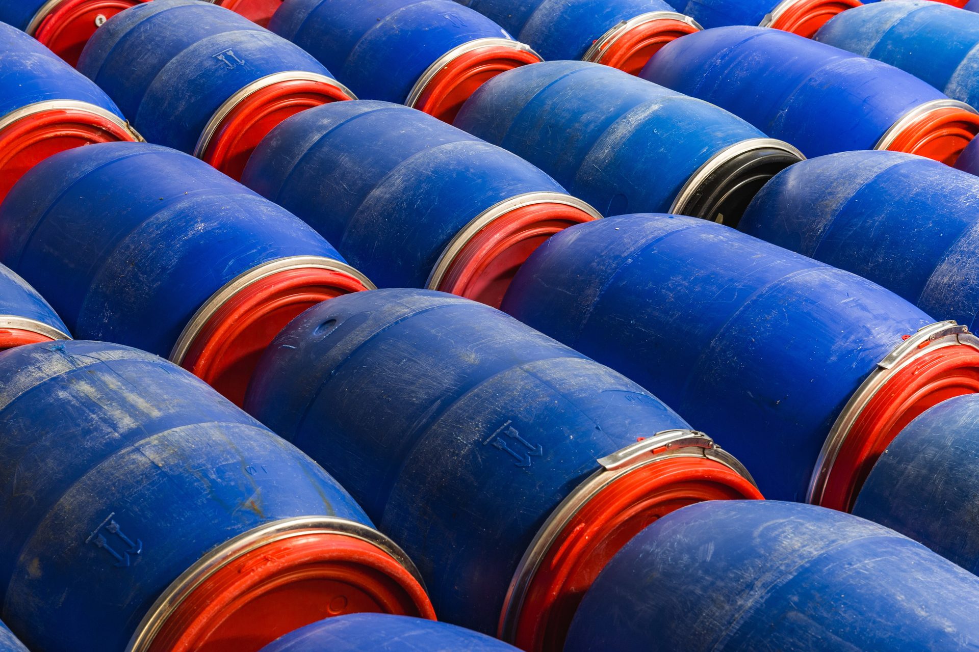 Rows of blue plastic drums with red lids and metal clamp rings, stacked on their sides
