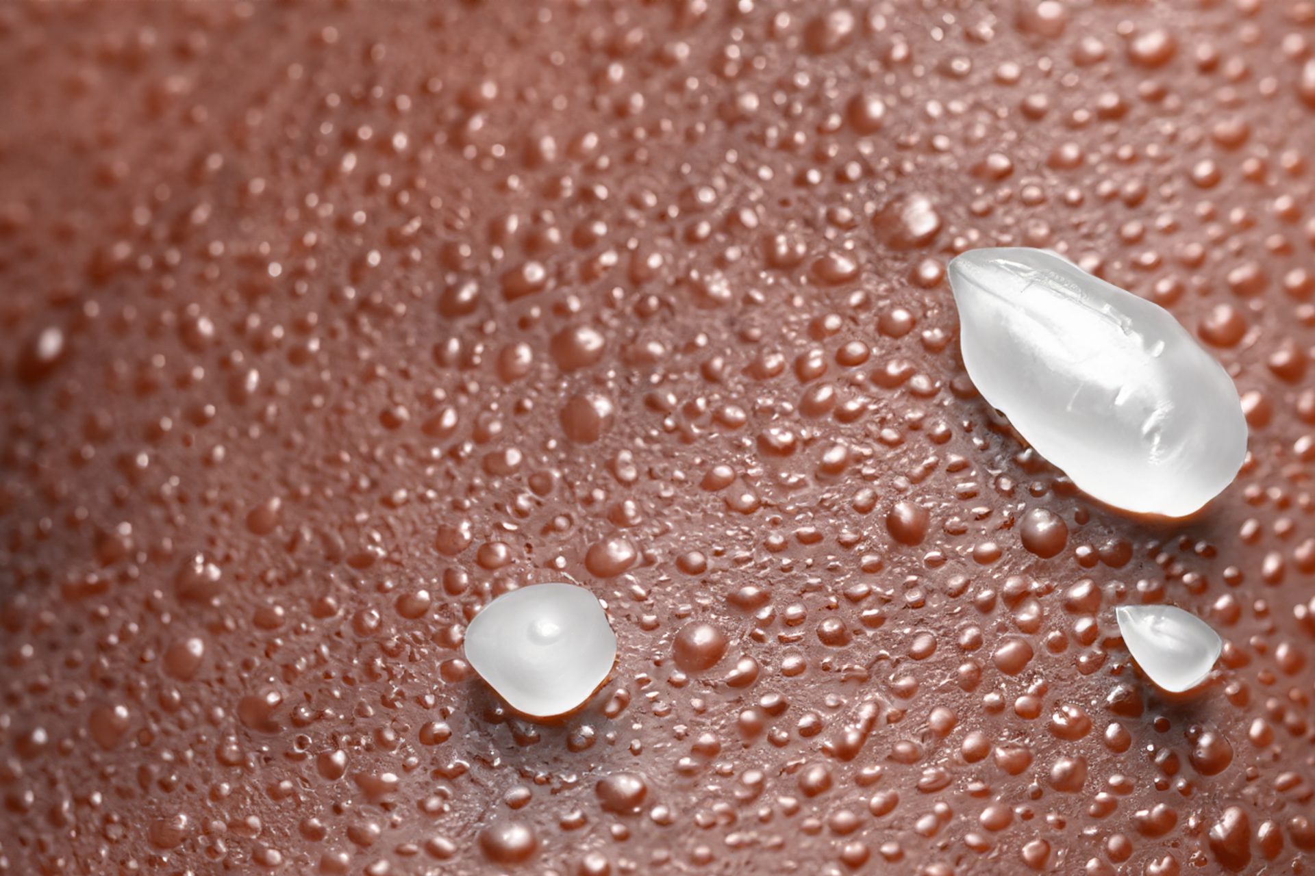 Clear gel droplets and small water beads on brown skin, close up