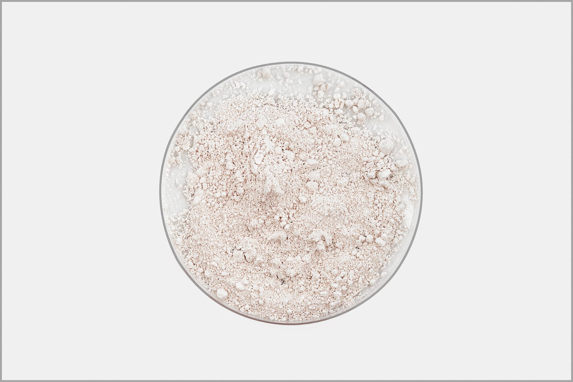 Top-down view of pale pinkish-white powder in a round glass dish on a light grey background