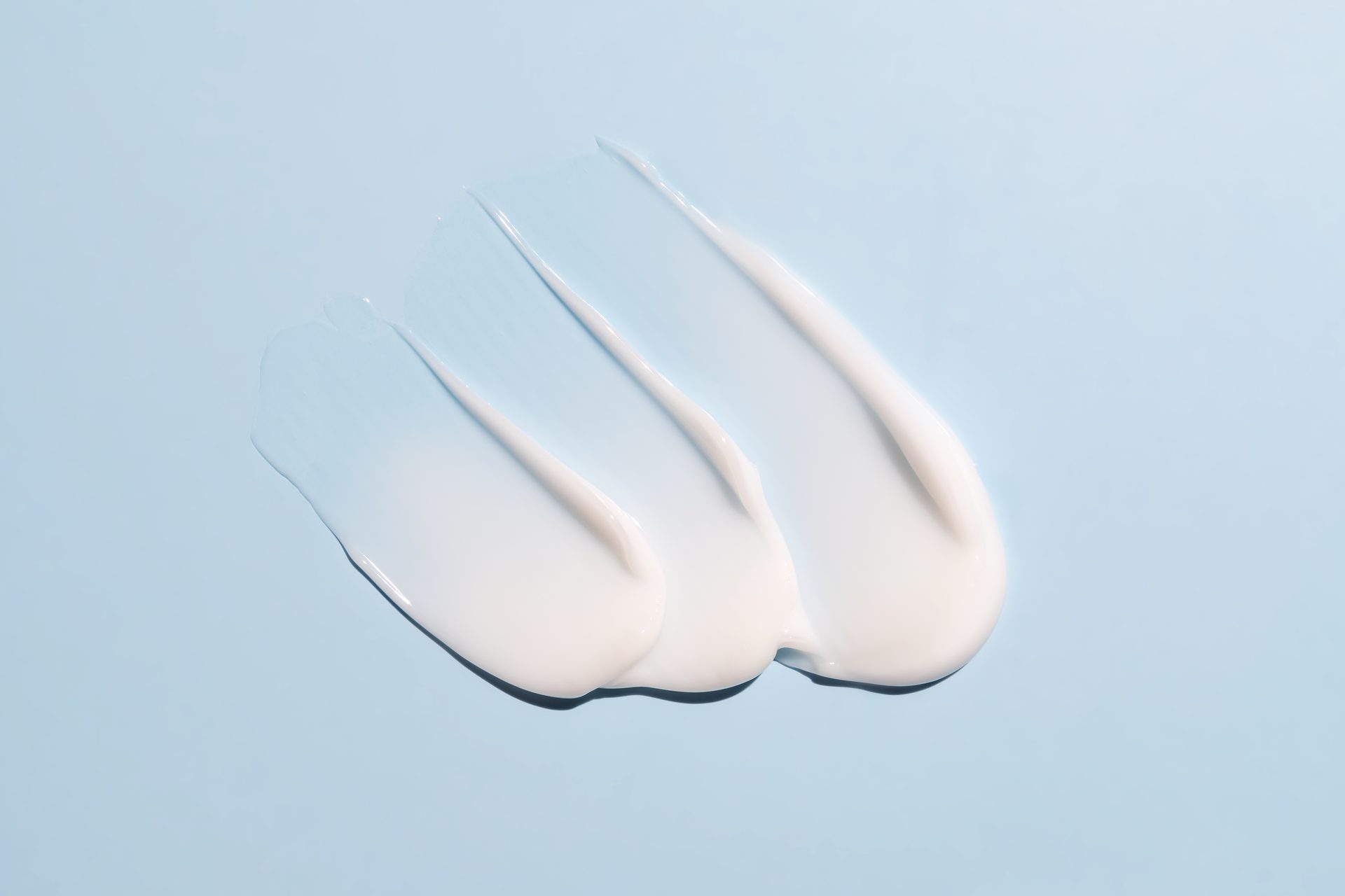Three smeared swatches of white cream on a pale blue background